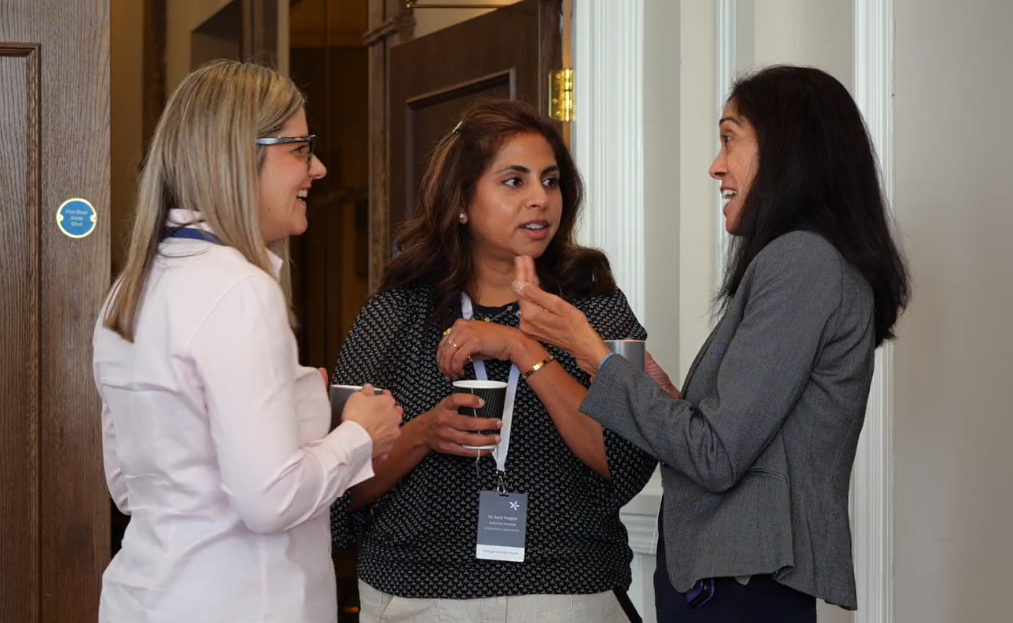Three women in conversation during a break at the Envisage Clinical Circle event, holding coffee cups and smiling in a relaxed, informal setting.